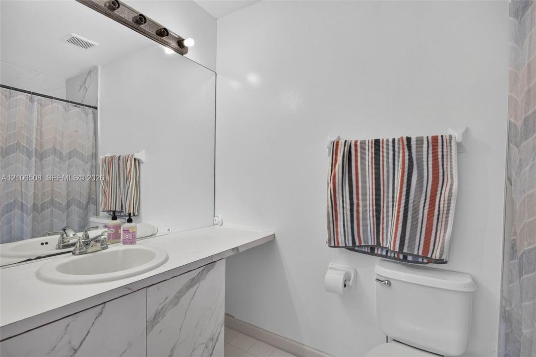 Vanity featuring a stone-finish facade, an integrated sink, an expansive wall-to-wall mirror, and a multi-bulb light fixture