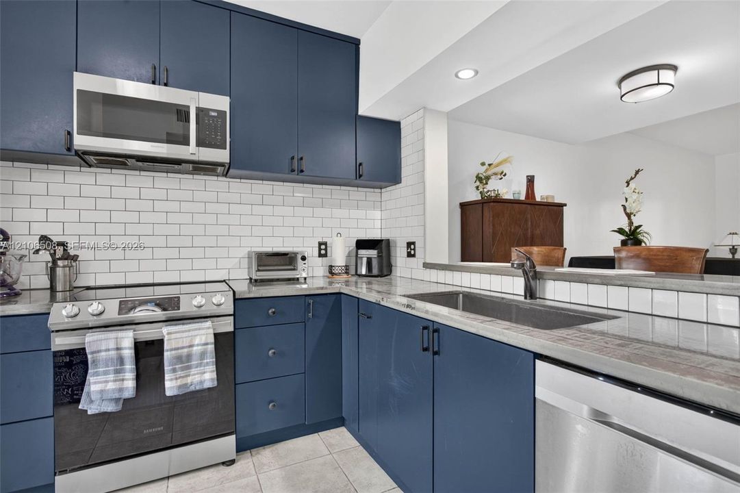 Kitchen featuring navy blue cabinetry, white subway tile backsplash, solid-surface countertops, stainless steel appliances, and a stainless steel undermount sink