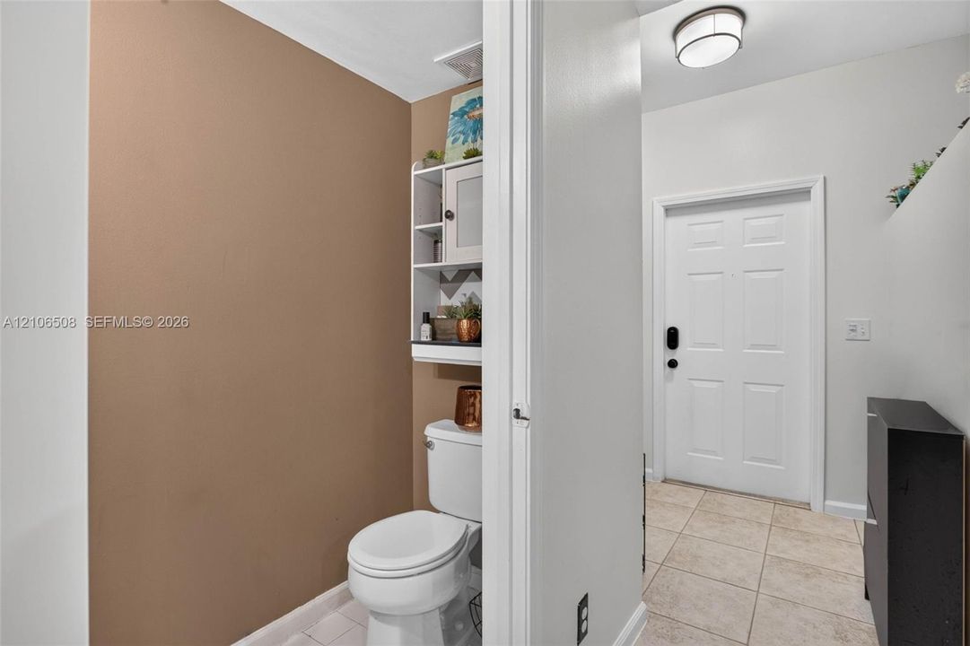 Ceramic tile flooring, white entry door with smart lock, flush-mount ceiling light fixture, and built-in wall shelving