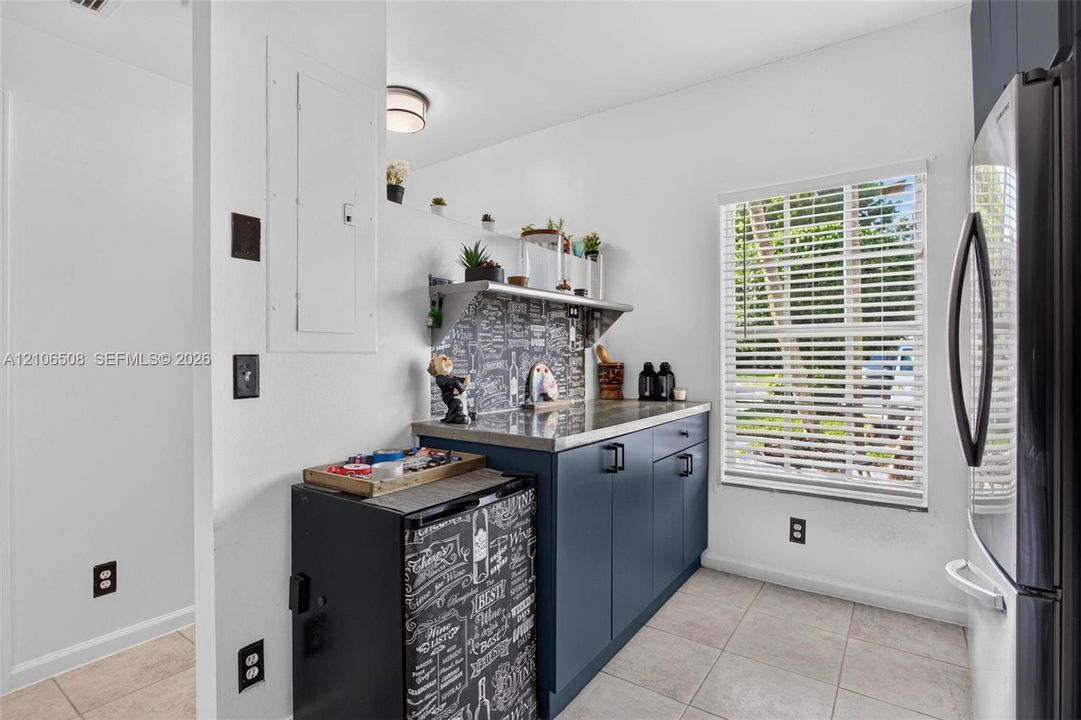 Navy blue base cabinetry, stone-finish countertop, patterned tile backsplash, stainless steel refrigerator, and ceramic tile flooring