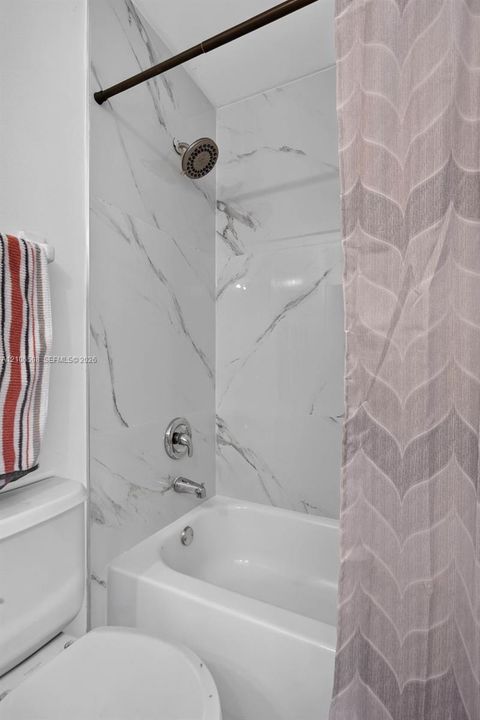 Tub and shower combination featuring full-height wall surround with veined stone-finish tile, wall-mounted shower head, and polished chrome hardware