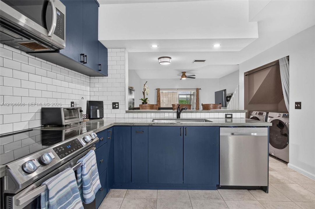 Kitchen featuring deep blue cabinetry, white subway tile backsplash, stainless steel appliances, stone-finish countertops, and recessed lighting