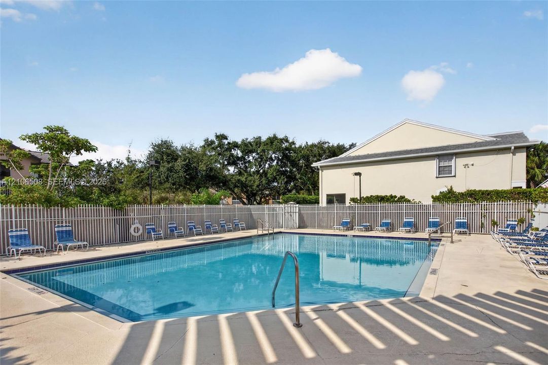 In-ground swimming pool featuring a concrete deck, metal perimeter fencing, and stainless steel pool ladder