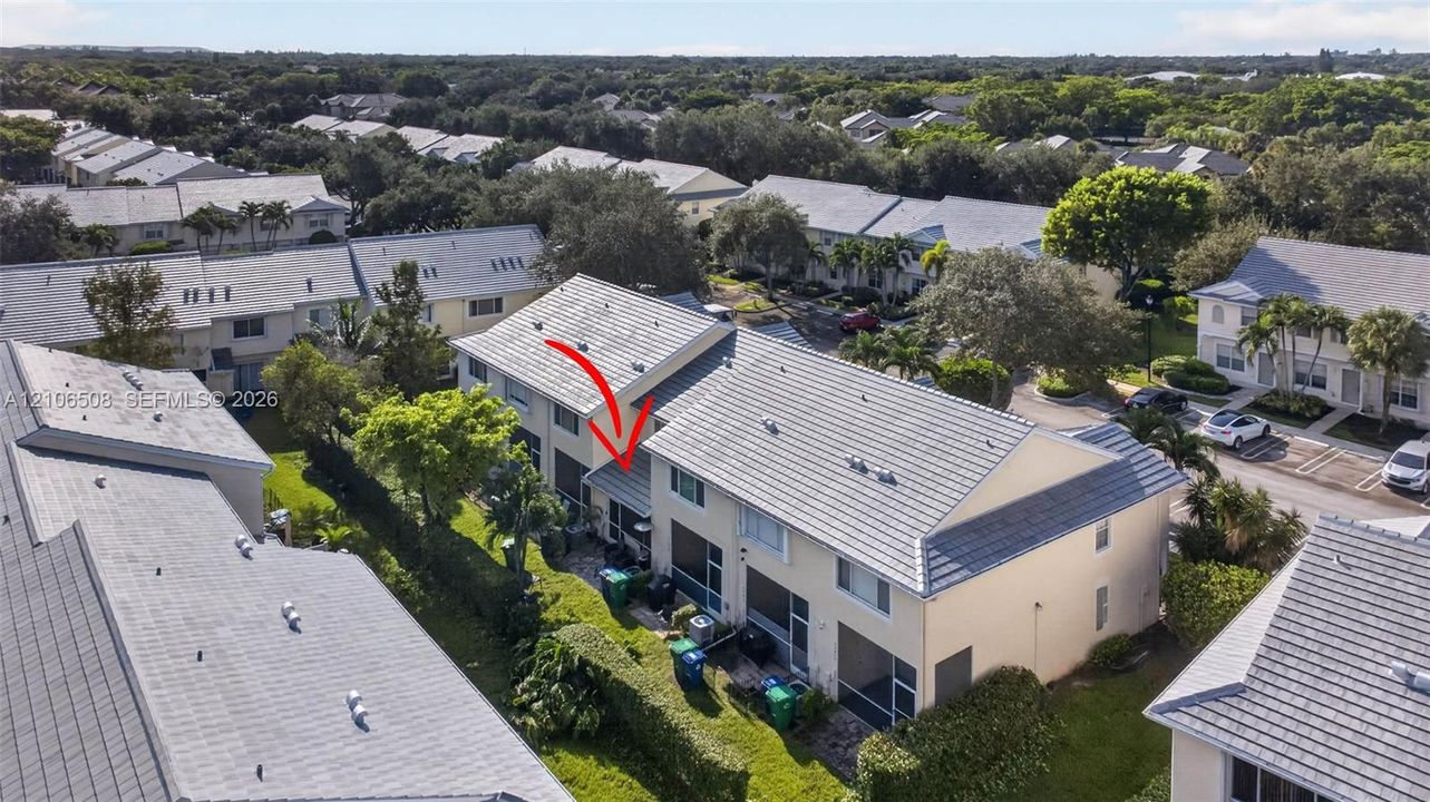 Aerial perspective of a multi-story residence featuring a light-colored stucco exterior, a neutral-toned tile roof, and a screened-in rear enclosure