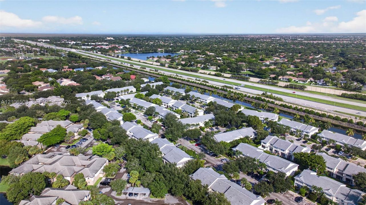 Aerial perspective of a multi-unit residential community featuring peaked roofing, mature shade trees, paved driveways, and expansive green space