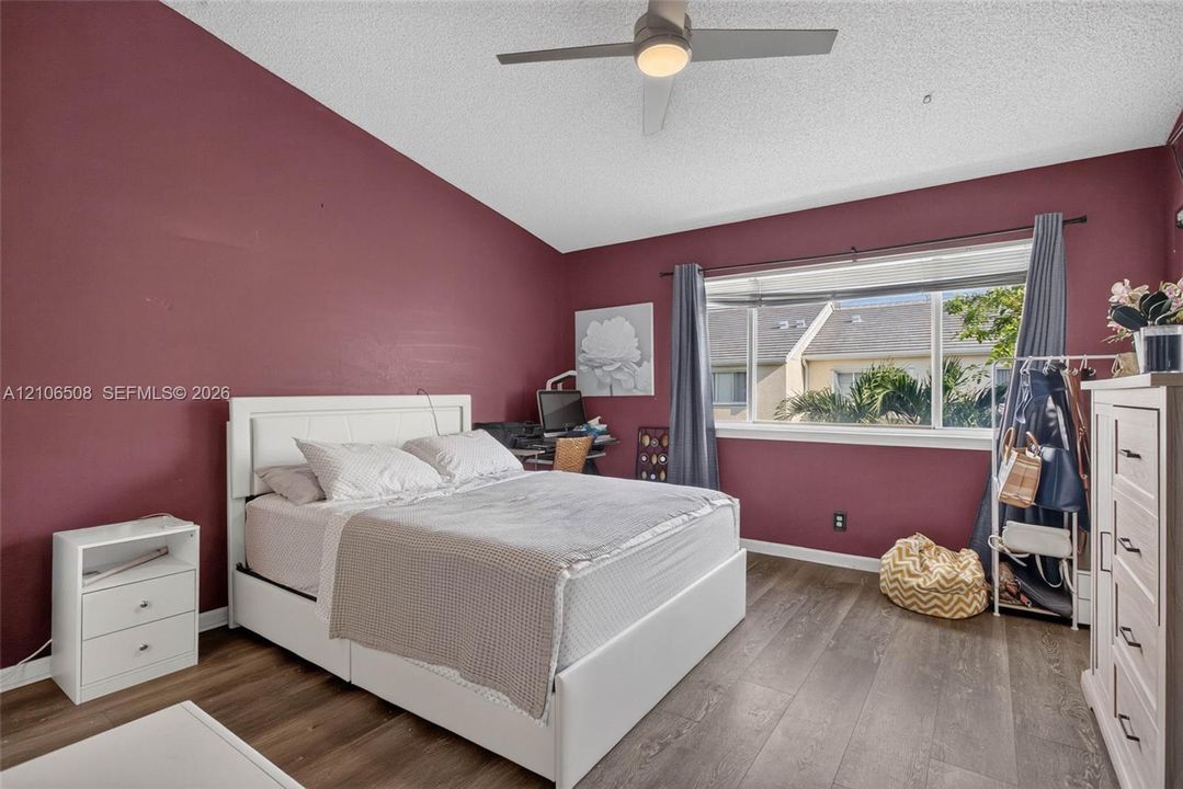 Vaulted ceiling, wood-finish flooring, and large window with exterior exposure, featuring an integrated ceiling fan
