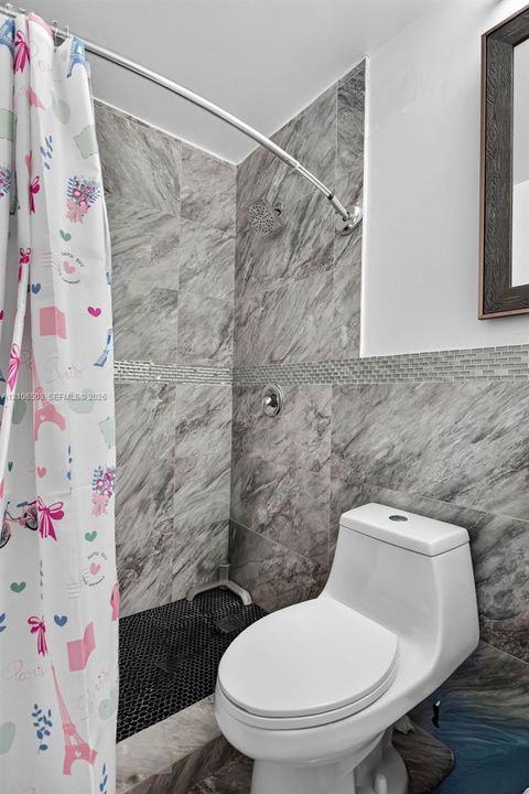 Bathroom featuring full-height large-format stone-patterned wall tile, a mosaic tile accent strip, a black penny tile shower floor, a rainfall shower head, and a dual-flush toilet
