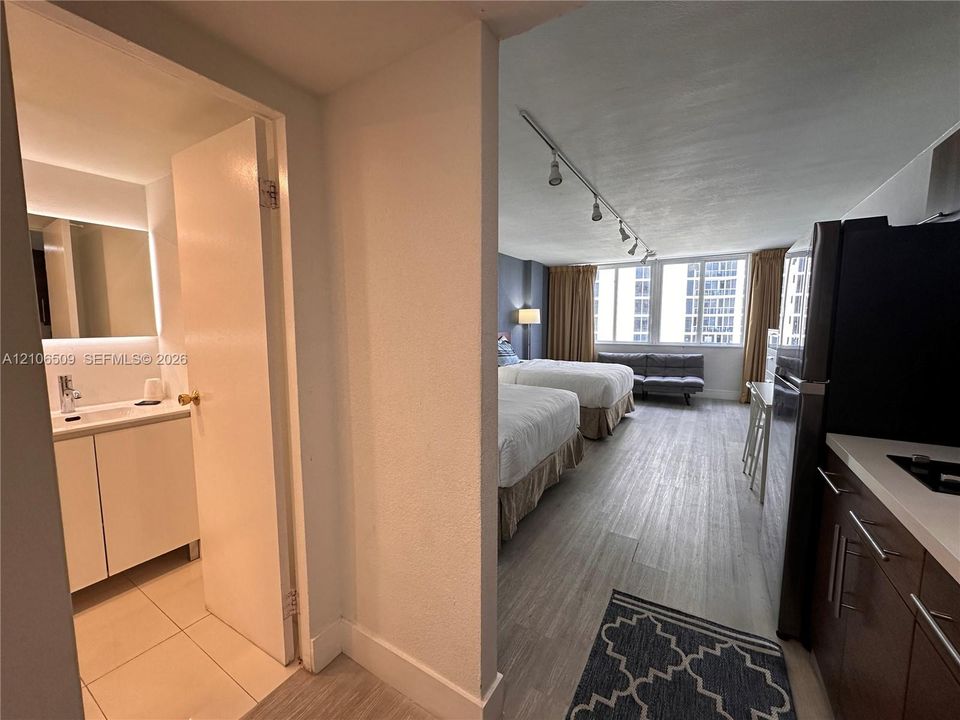 Bathroom featuring a vanity with integrated sink and backlit mirror, wood-finish flooring, track lighting, and a kitchenette equipped with cabinetry and stone-surfaced countertops