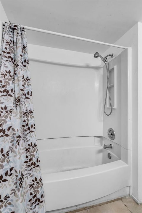 Bathtub and shower combination featuring a white surround, integrated shelving, handheld showerhead, and metal hardware