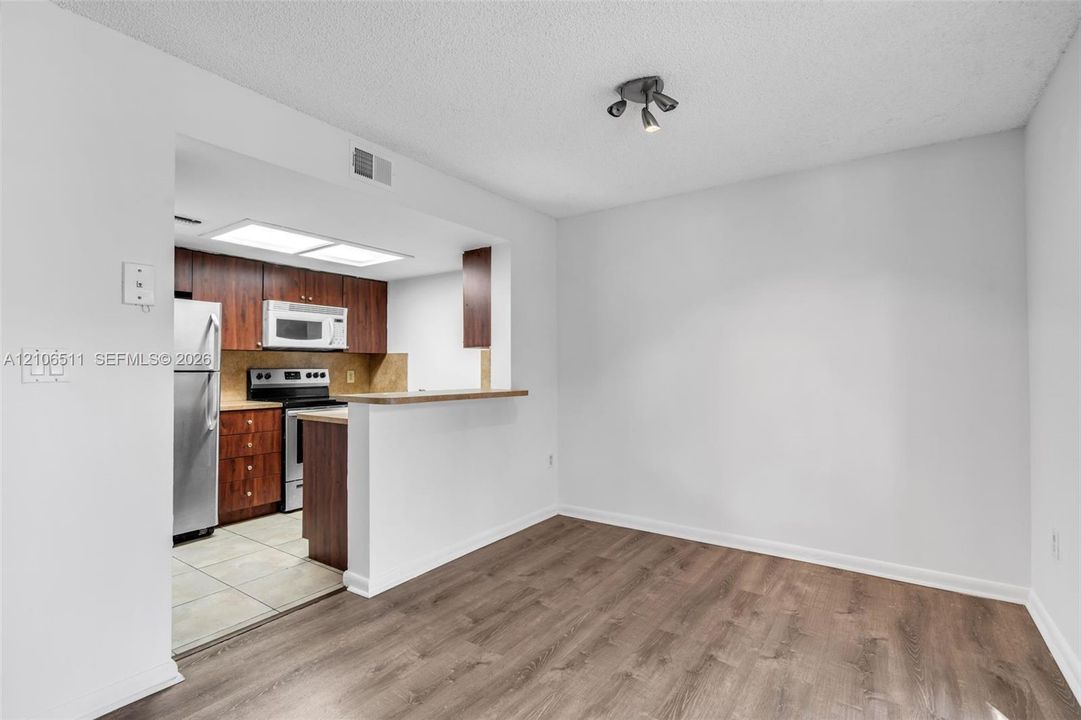 Kitchen featuring wood-finish cabinetry, stainless steel appliances, neutral tile flooring, wood-finish flooring, and a breakfast bar