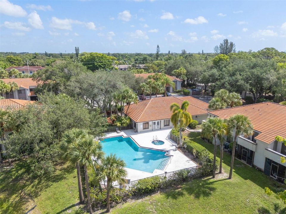 Community pool featuring an attached spa, expansive concrete pool deck, tile roofing, and mature palm trees