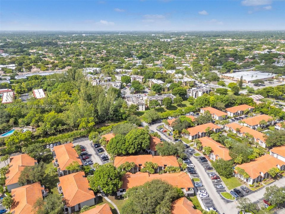 Aerial perspective of a multi-building residential complex featuring terra cotta-style tile roofing, mature landscaping, paved surface parking, and shared outdoor pool area