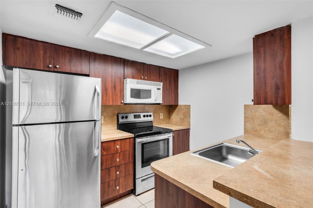 Kitchen featuring dark-toned wood cabinetry, stainless steel refrigerator and range, integrated microwave, and neutral-toned countertops with a stainless steel sink