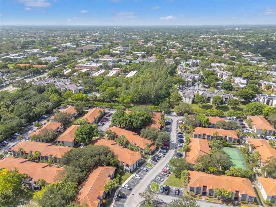 Aerial perspective of a multi-unit complex featuring terra-cotta tile roofing, mature landscaping, designated paved parking areas, and a community tennis court