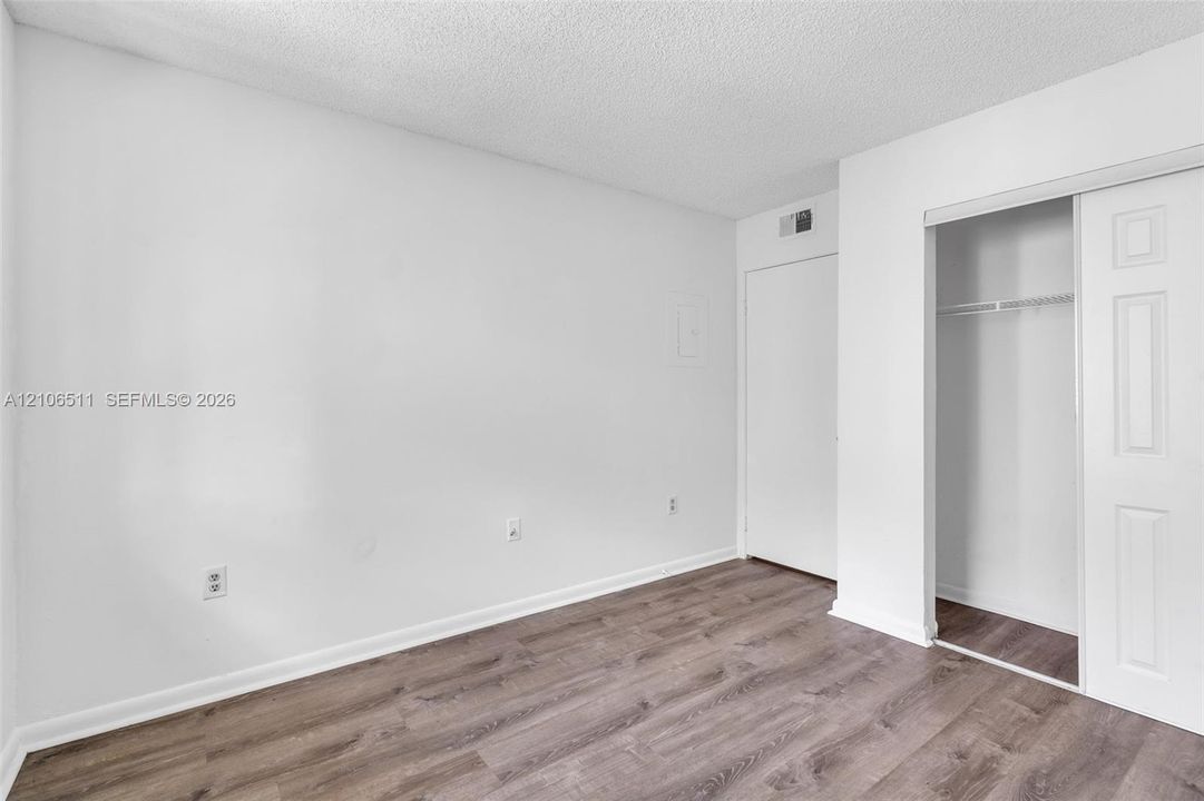 Room with wood-finish flooring, white walls, and a closet with sliding paneled doors