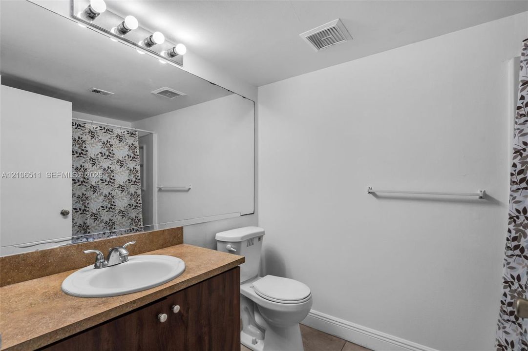 Bathroom featuring a wood-finish vanity with a solid-surface countertop, an integrated oval sink, a full-width wall mirror, and a multi-bulb light fixture