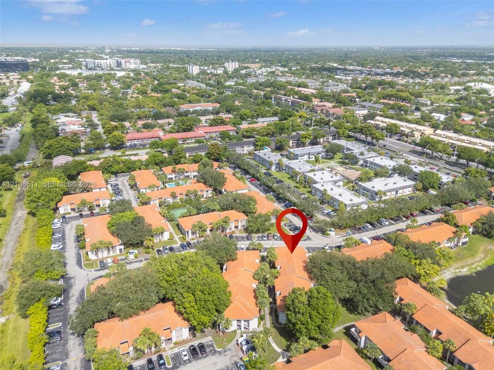 Aerial view featuring a multi-unit residential complex with terracotta-style roof tiles, mature landscaping, and dedicated surface parking