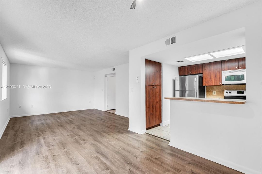 Open-concept interior featuring wood-finish flooring, kitchen cabinetry with a dark wood finish, stainless steel refrigerator, and recessed kitchen lighting