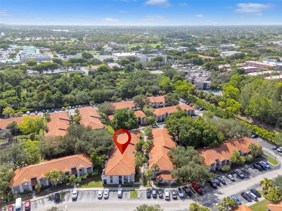 Aerial perspective of multi-family residential complex featuring terracotta-tiled roofs, stucco exterior finish, mature shade trees, and surface parking