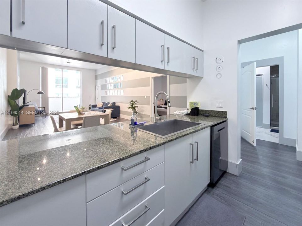 Kitchen featuring stone countertops, stainless steel undermount sink, gooseneck faucet, light-finish cabinetry with metallic hardware, and dishwasher