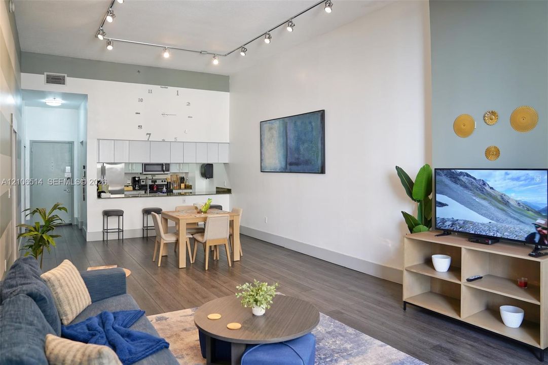 High ceilings featuring a linear track lighting system, dark wood-finish flooring, and a kitchen with overhead cabinetry