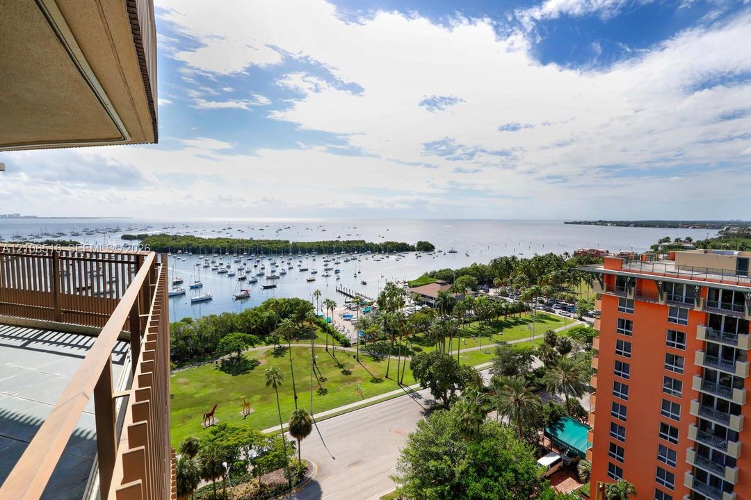 Elevated outdoor balcony with metal railing, overlooking a coastal expanse, harbor, and landscaped green space