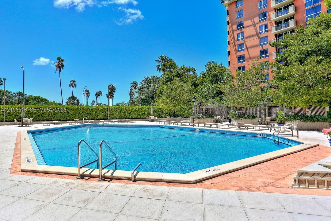 In-ground swimming pool featuring a geometric perimeter, masonry coping, and metal entry handrails, complemented by expansive stone-paver decking and mature landscaping