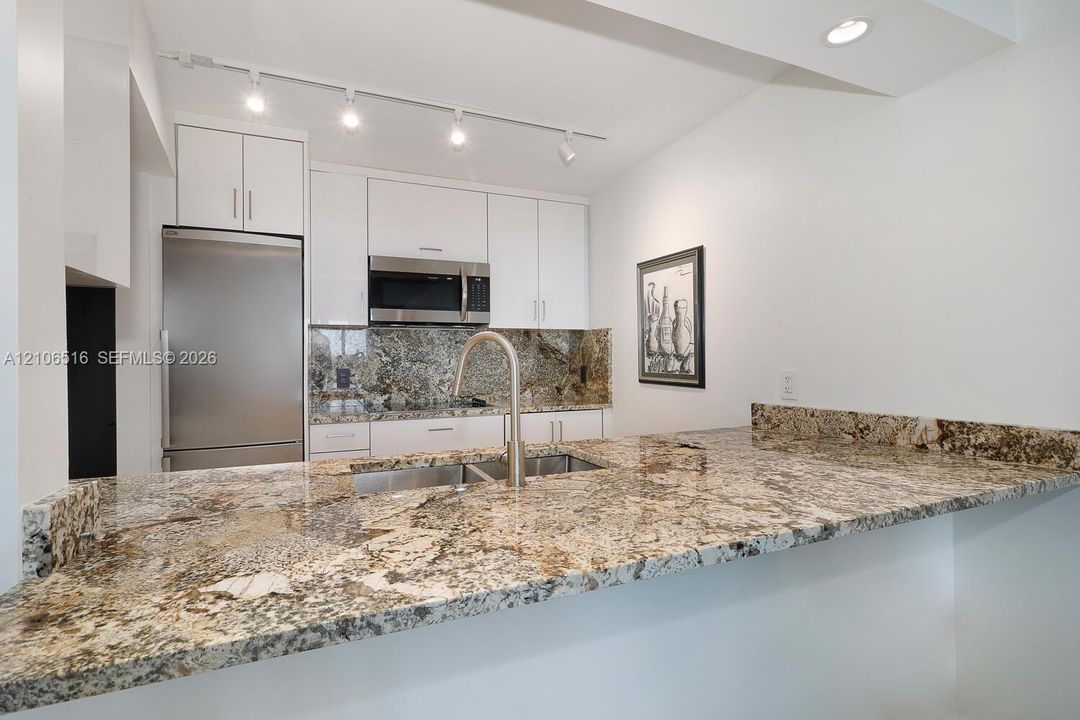 Kitchen featuring stone countertops, stainless steel appliances, white cabinetry, a dual-basin undermount sink with a gooseneck faucet, and overhead track lighting