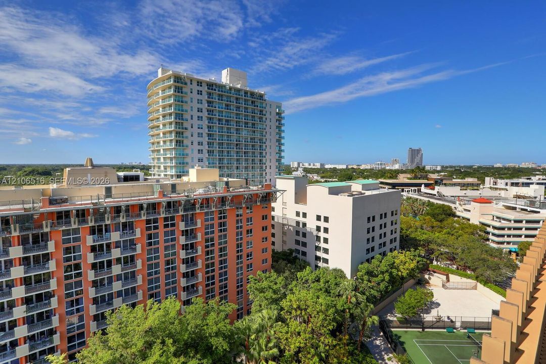 High-rise residential exterior with glass-railed balconies and a dedicated on-site tennis court nestled among mature landscaping