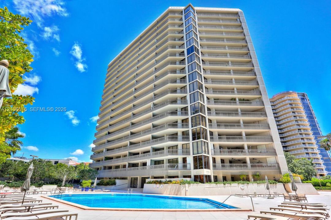 High-rise residential building featuring expansive private balconies, floor-to-ceiling glass paneling, and an outdoor swimming pool with a paved surround