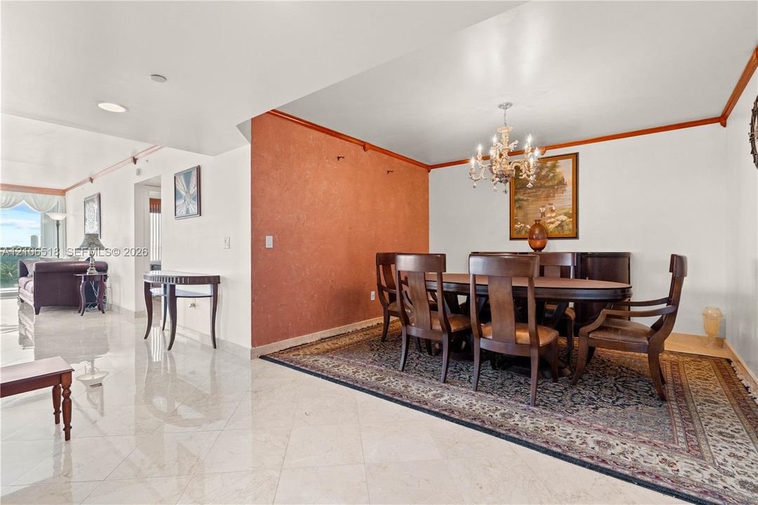 Polished stone flooring, textured accent wall, crown molding, and a tiered crystal chandelier
