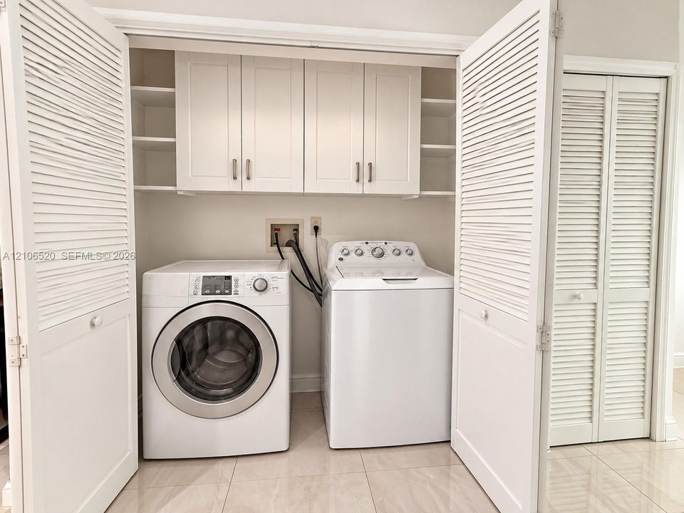 Laundry area featuring white shaker-style wall cabinetry, open shelving, tile flooring, and white louvered bifold doors