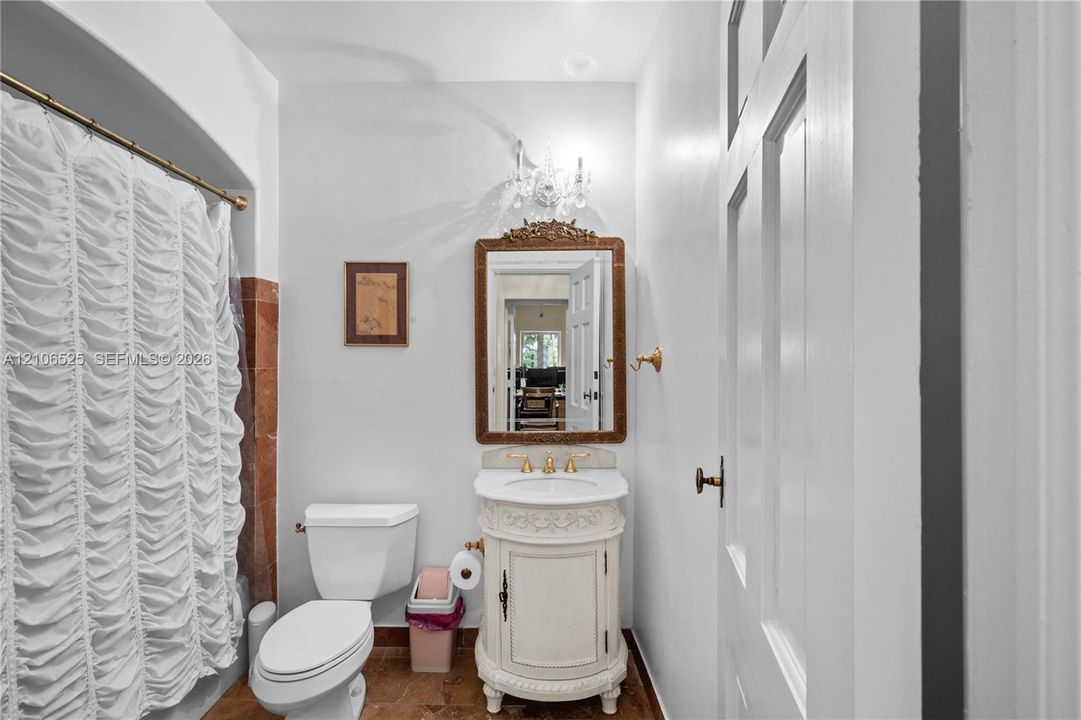 Decorative vanity with carved detailing, stone countertop, gold-toned faucet, wall-mounted light fixture, and framed wall mirror