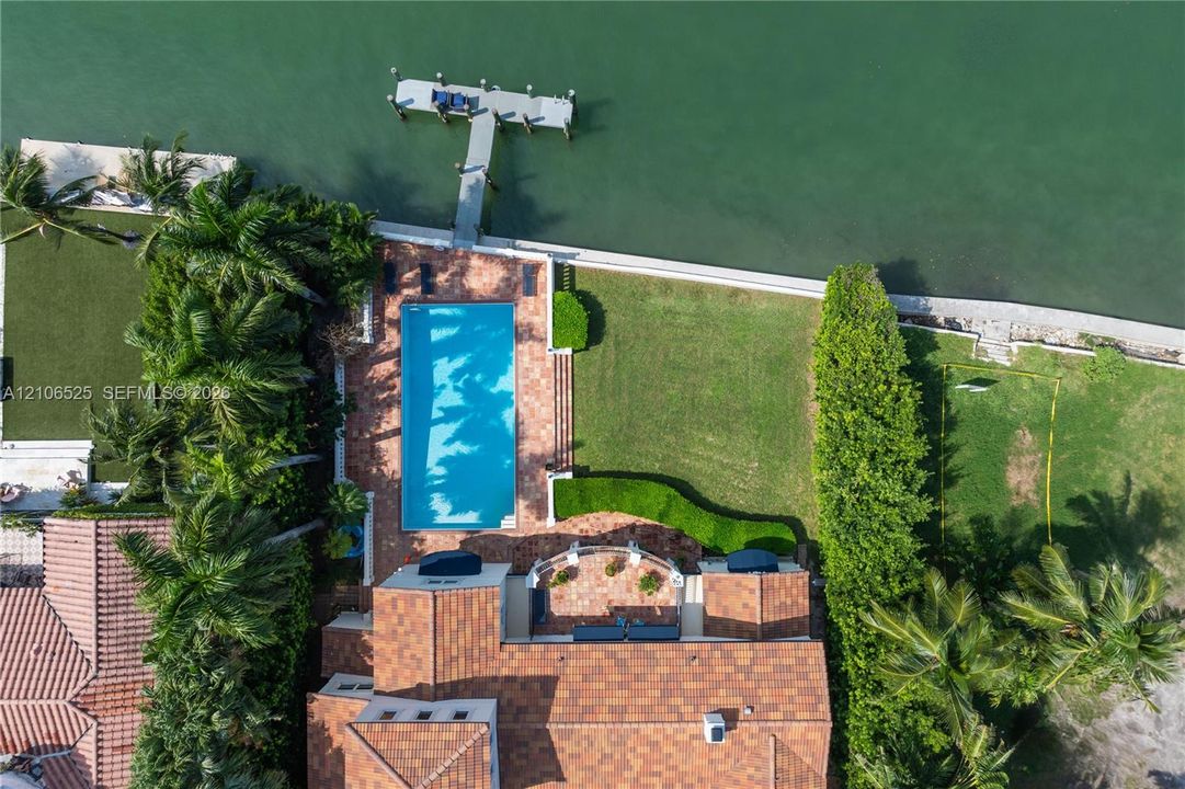 Waterfront property featuring a rectangular swimming pool, terracotta-tiled patio, private boat dock, and manicured lawn