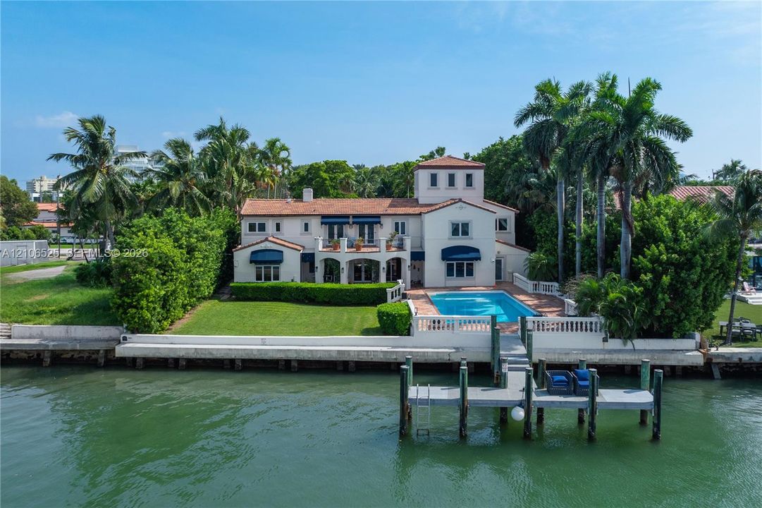 Waterfront residence featuring a private dock, swimming pool, tiled roof, and expansive lawn