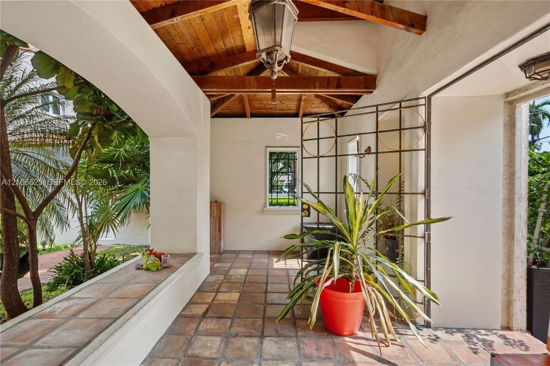 Covered patio featuring an exposed wood-beam ceiling, tile flooring, built-in bench seating, and an ornamental metal gate