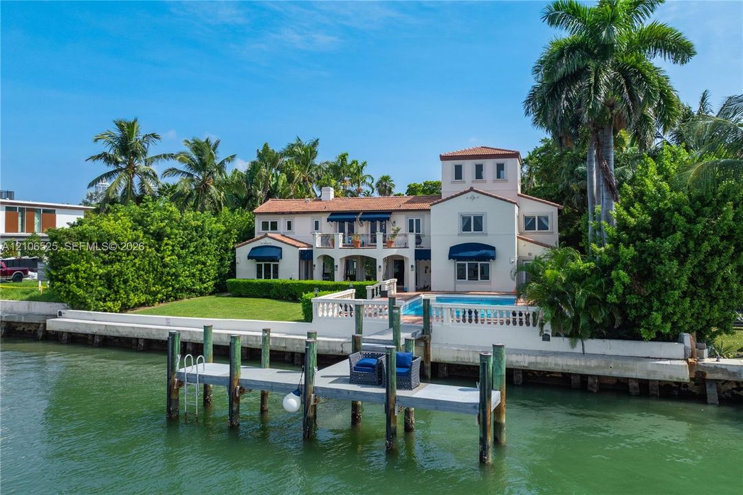 Waterfront residence featuring a private dock, swimming pool, second-story balcony, and terracotta-style roof tiles