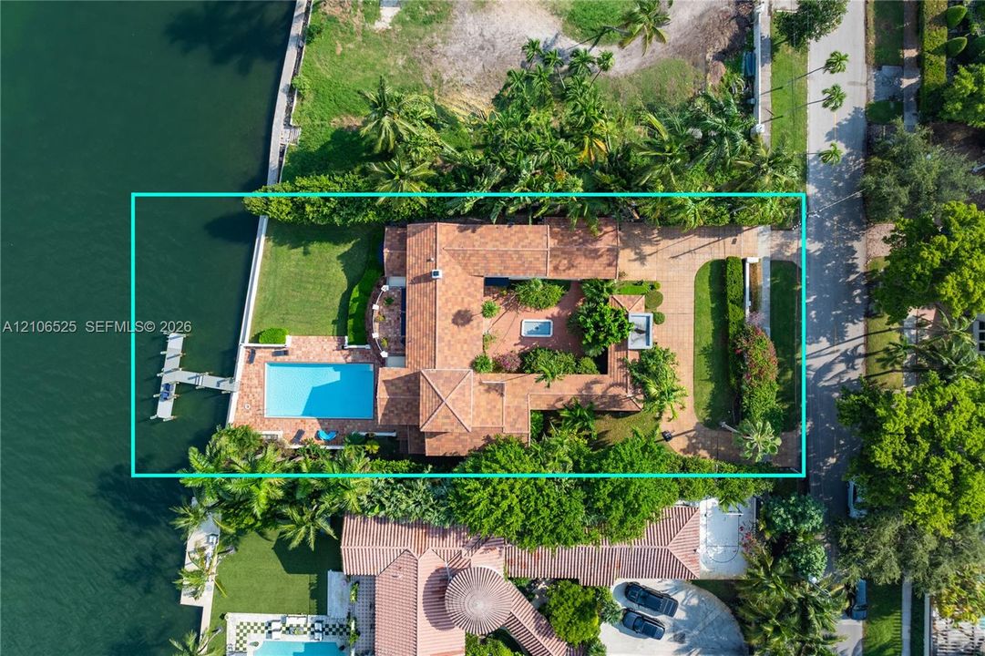 Waterfront estate featuring a private dock, rectangular swimming pool, terracotta tile roof, brick-paved courtyard, and mature landscaping