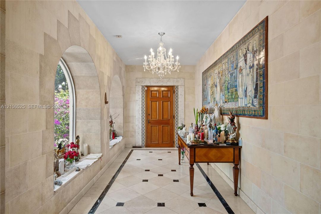 Entryway featuring natural stone block walls, arched window alcoves, tile flooring with decorative stone insets, a crystal chandelier, and a solid wood door