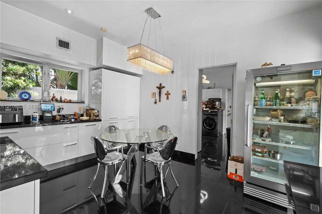 Glossy cabinetry featuring integrated storage, black stone countertops, high-gloss tile flooring, and a rectangular crystal-accented pendant light fixture