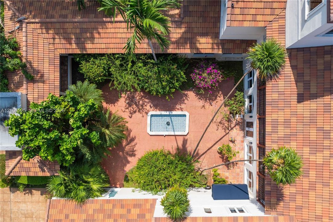 Enclosed courtyard featuring a tiled roof, central rectangular fountain, landscaped greenery, and terracotta-style paving