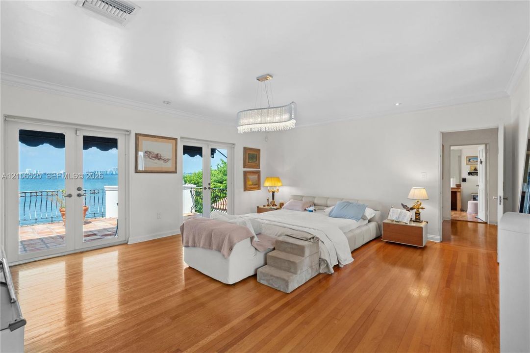 Spacious interior featuring wood-finish flooring, dual sets of French doors, crown molding, a decorative crystal chandelier, and a balcony with water scenery