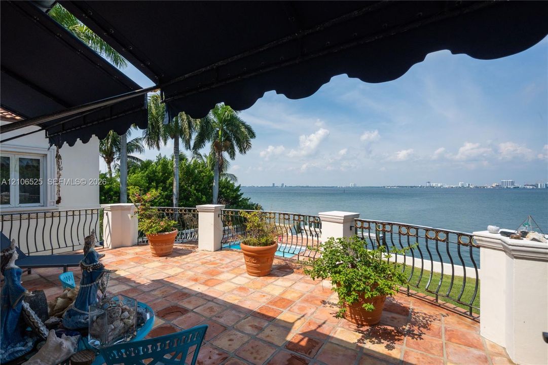 Terrace featuring terracotta tile flooring, wrought iron perimeter railing, retractable fabric awning, and masonry pillars