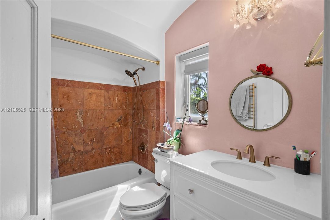 Bathroom featuring a white vanity with an integrated basin, stone tile tub surround, gold-tone hardware, and a crystal chandelier