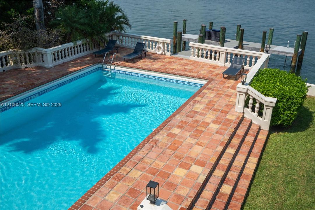 In-ground swimming pool featuring a terra-cotta tile deck, a balustrade perimeter railing, and a private wooden dock extending over the water