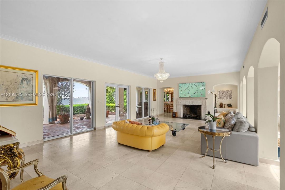 Living area featuring large-format stone tile flooring, three sets of sliding glass doors, a stone-surround fireplace, arched alcoves, and a tiered crystal chandelier