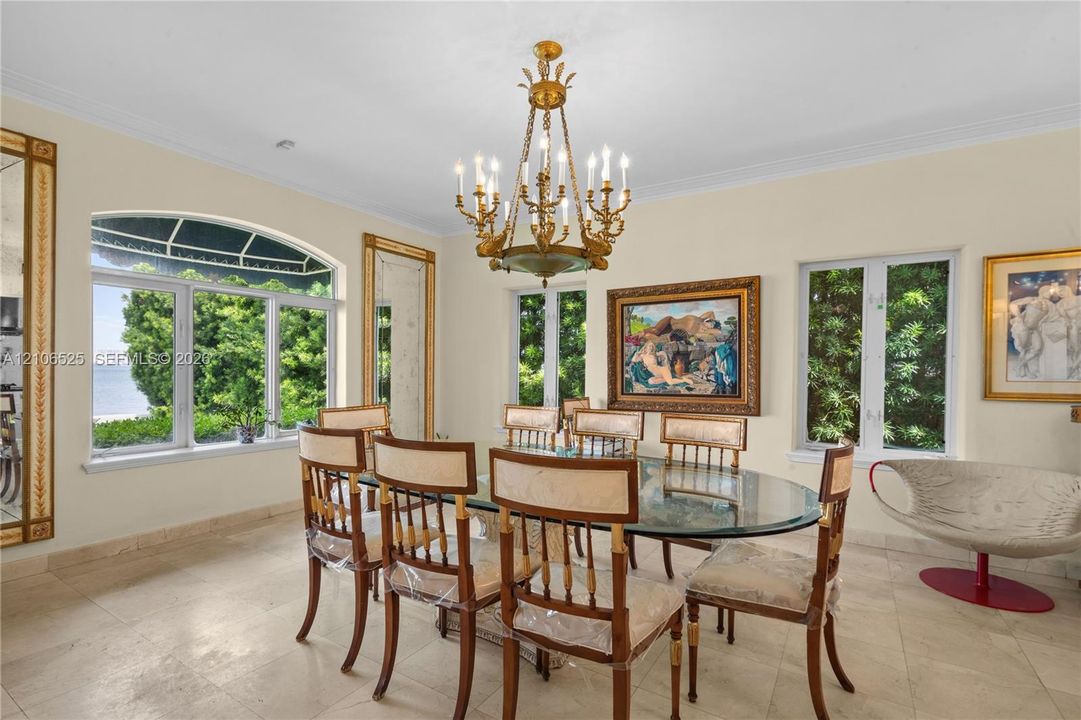 Ornate brass chandelier, natural stone flooring, arched window with multi-pane glazing, and framed wall mirrors