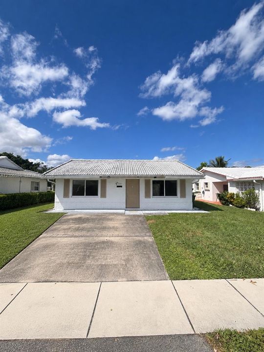 Single-story exterior featuring a white painted brick facade, concrete tile roof, shuttered windows, and a dedicated concrete driveway