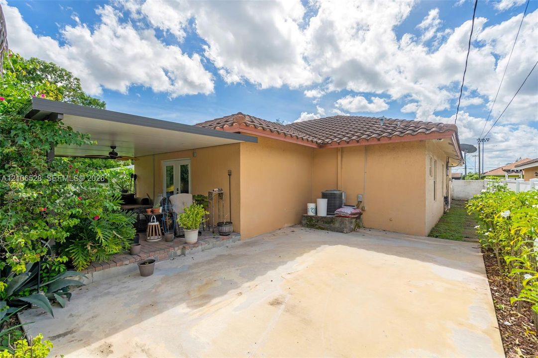 Covered concrete patio with a brick border, concrete hardscaping, tile roofing, and stucco exterior