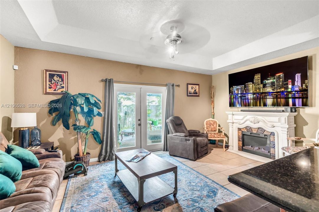 Tray ceiling with central light fixture, fireplace featuring a decorative mantle, and glass-paneled double doors